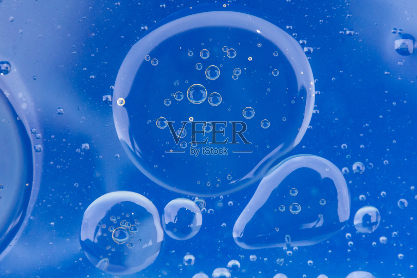 大的油泡聚集在带有亮蓝色背景的水中。照片摄影图片