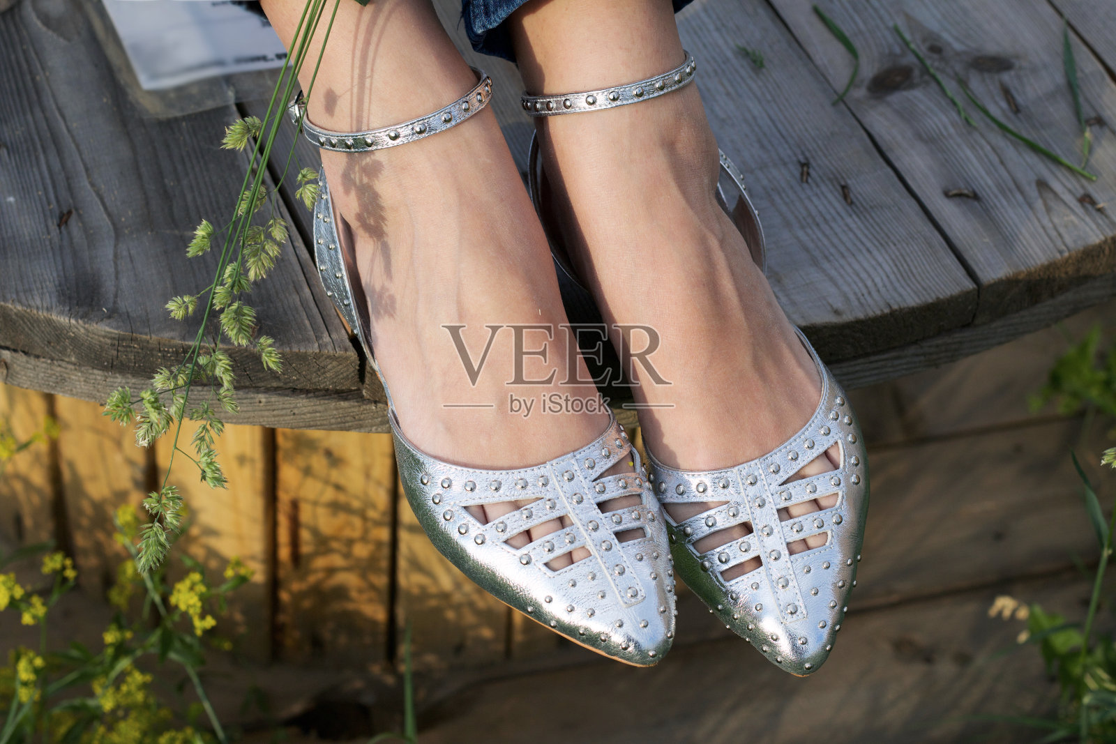 一个女孩坐在木制电缆卷轴上。脚和凉鞋特写。照片摄影图片