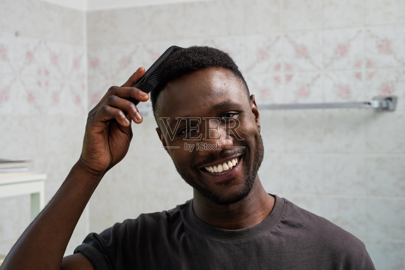 英俊的黑人男人微笑和梳头发在浴室照片摄影图片