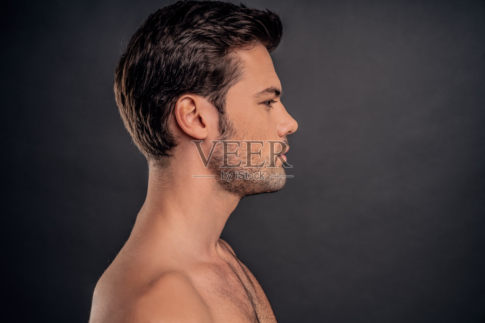 英俊的留着胡子的年轻人孤立无援。一个赤裸上身的肌肉男正站在灰色背景上。男性保健的概念。照片摄影图片