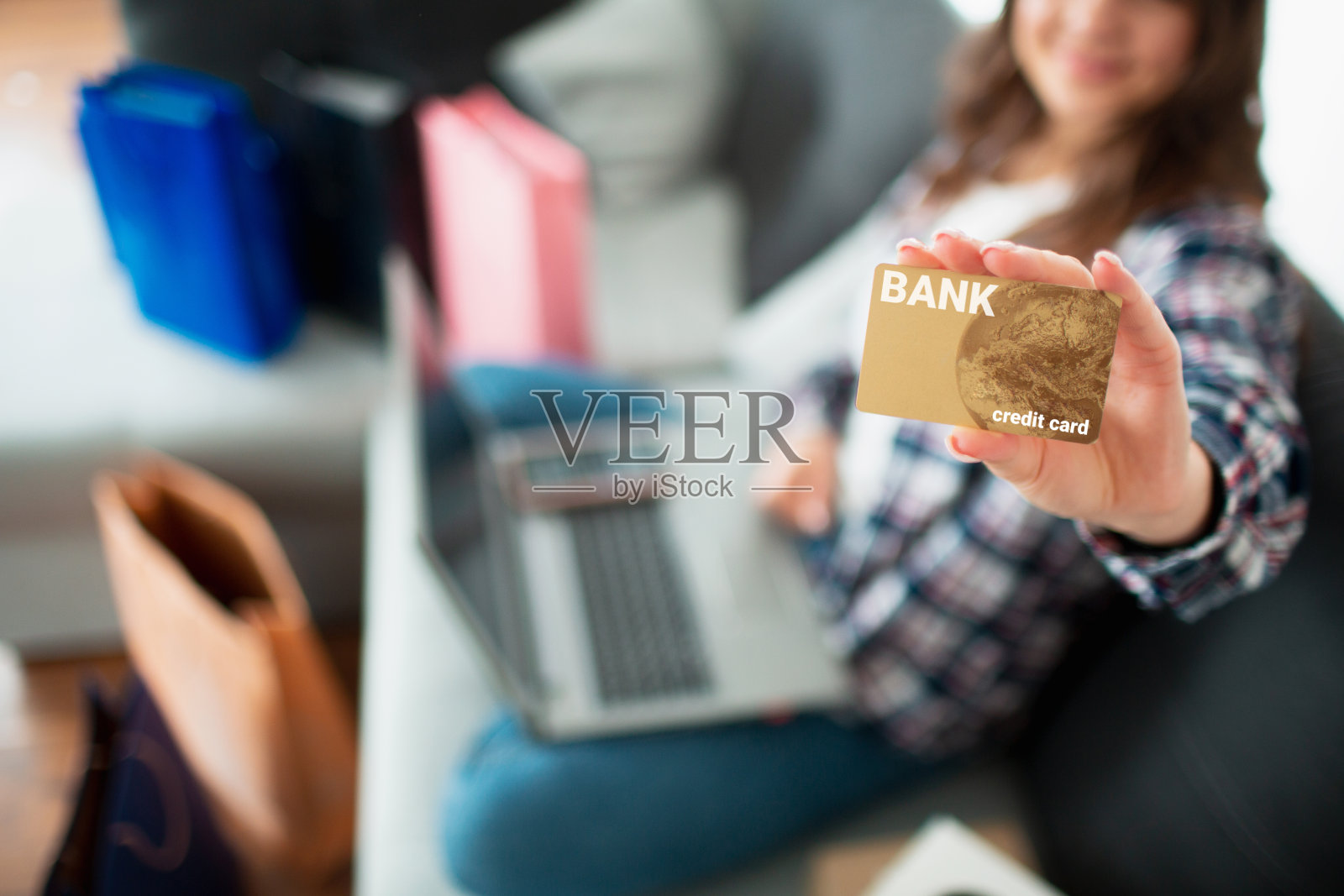 买家看着屏幕，手里拿着一张信用卡。一个年轻女子用笔记本电脑在网上买了很多东西。她在等送货上门。特写信用卡金卡。照片摄影图片