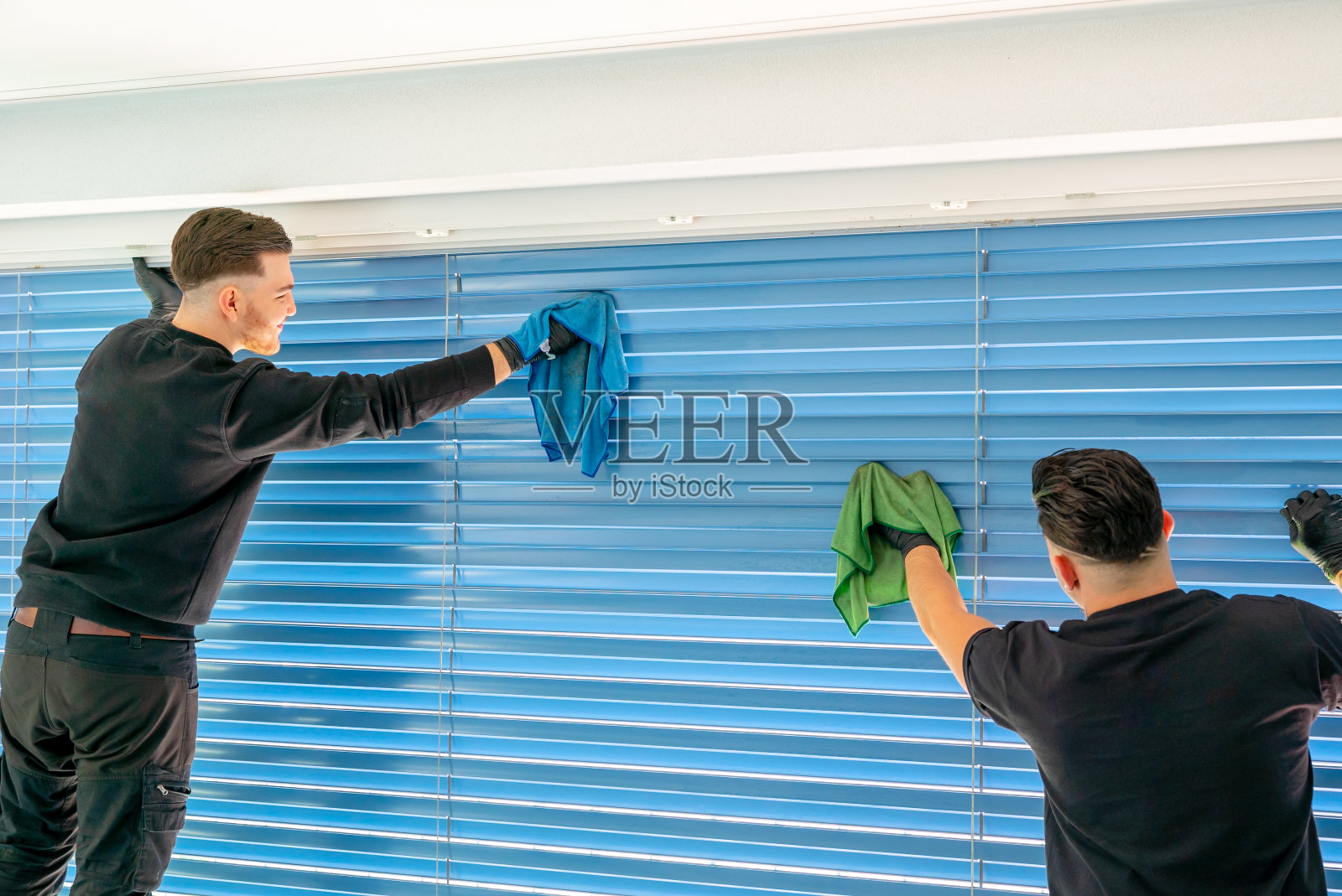 两名男性专业清洁工正在用超细纤维布清洁大窗户前面的蓝色百叶窗照片摄影图片