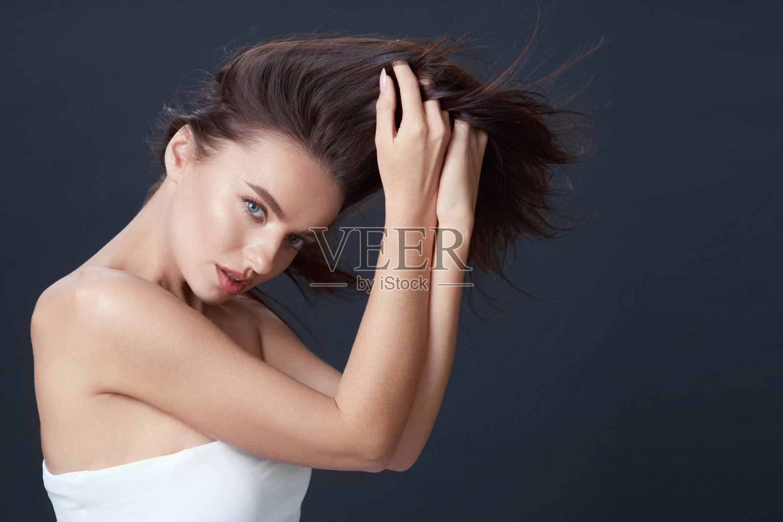 美丽的女孩。女人触摸头发肖像。蓝眼睛的深色皮肤光滑完美的皮肤和自然的化妆在黑色的背景。年轻的模特看着相机。照片摄影图片