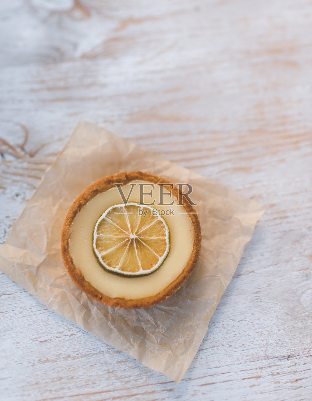 在白色木质背景上点缀着一片酸橙的柠檬奶油脆皮馅饼照片摄影图片
