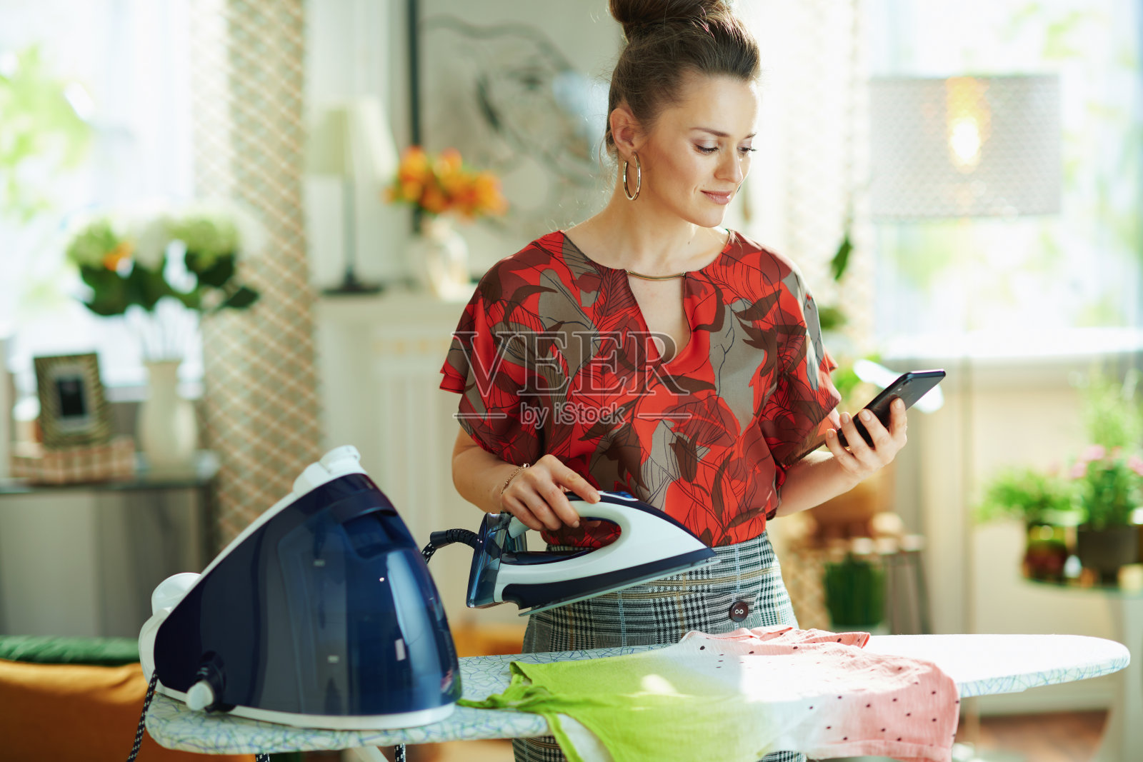 正在用智能手机熨烫衣服的优雅女人照片摄影图片