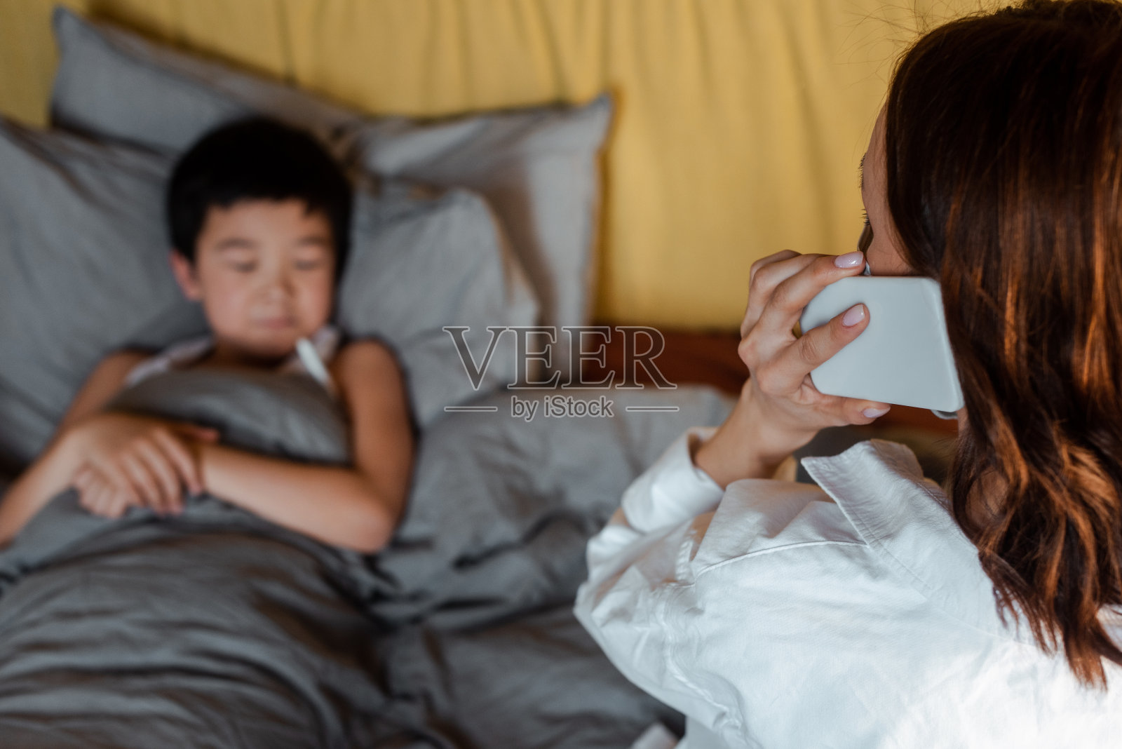 生病的亚洲男孩躺在床上，而母亲打电话给医生隔离照片摄影图片