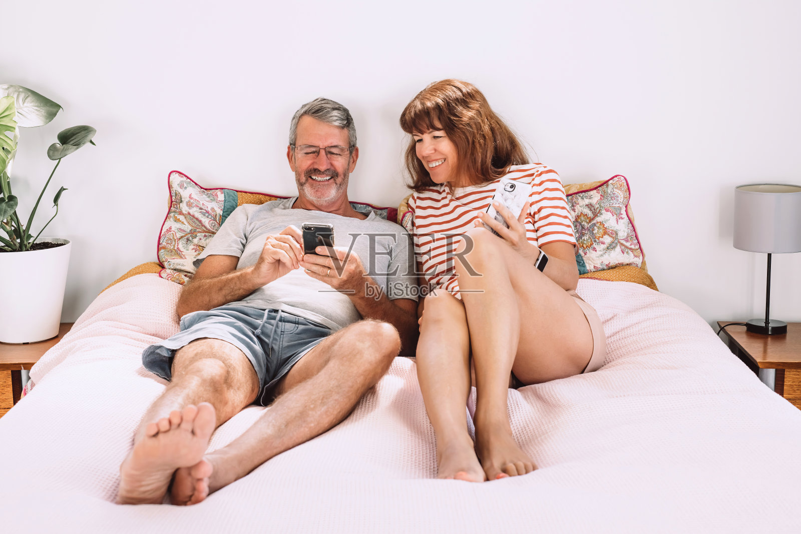一对中年夫妇躺在床上玩手机，大笑。照片摄影图片