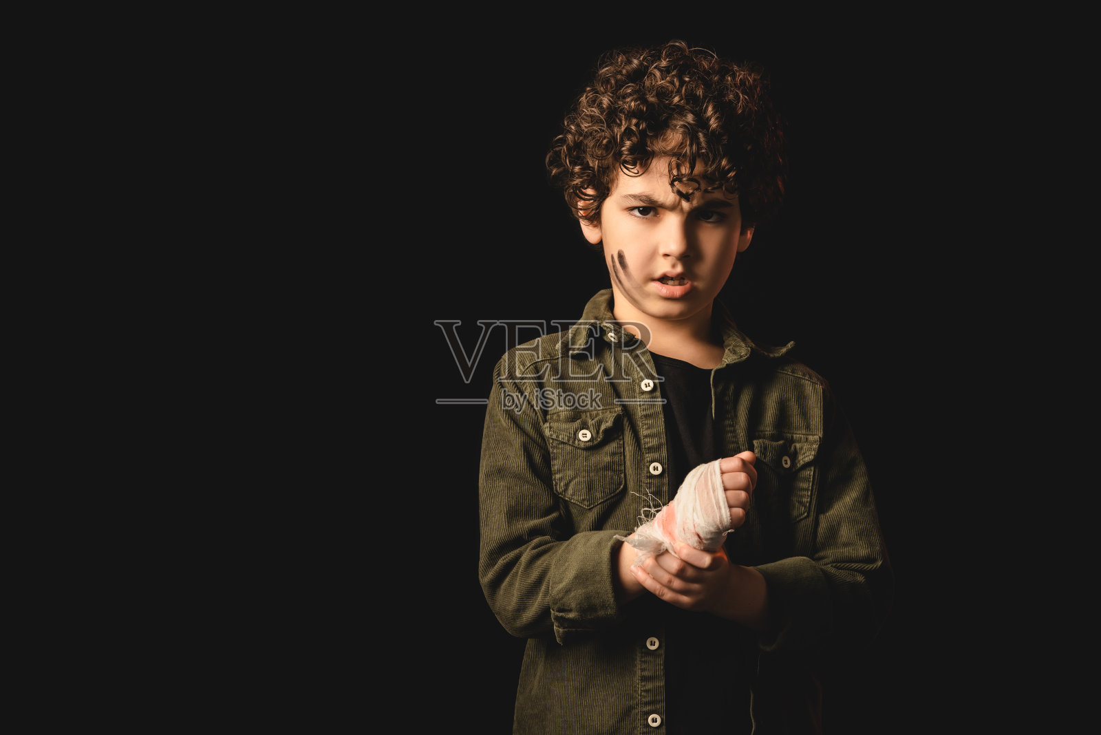 被冒犯的穆斯林孩子，肮脏的脸触摸受伤的手，绷带隔离在黑色照片摄影图片