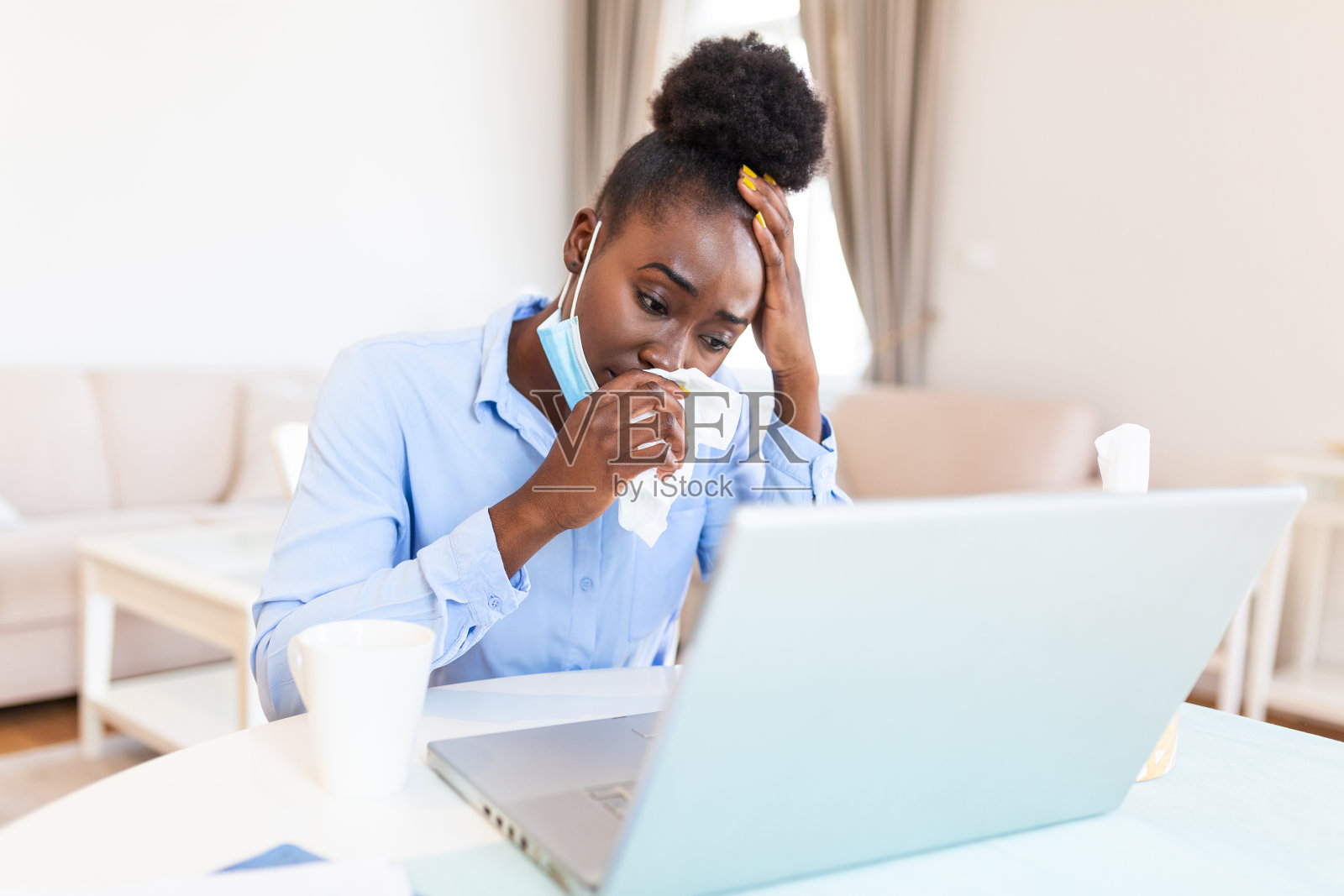 失意的非洲女商人坐在办公室里用纸巾擤鼻涕。一名女商人在她的家庭办公室里工作，同时遭受过敏或疾病的折磨照片摄影图片