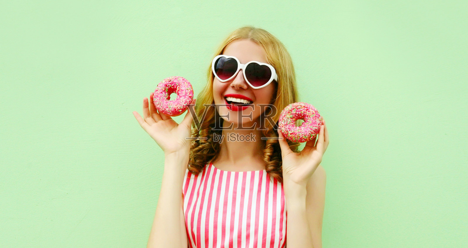 快乐微笑的年轻女子肖像与两个甜甜圈在一个绿色的背景照片摄影图片