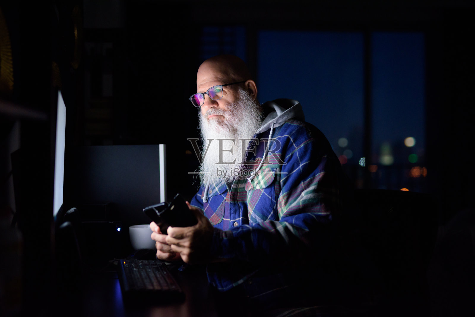 成熟的秃头胡子嬉皮士在深夜的黑暗中在家思考和使用电话照片摄影图片