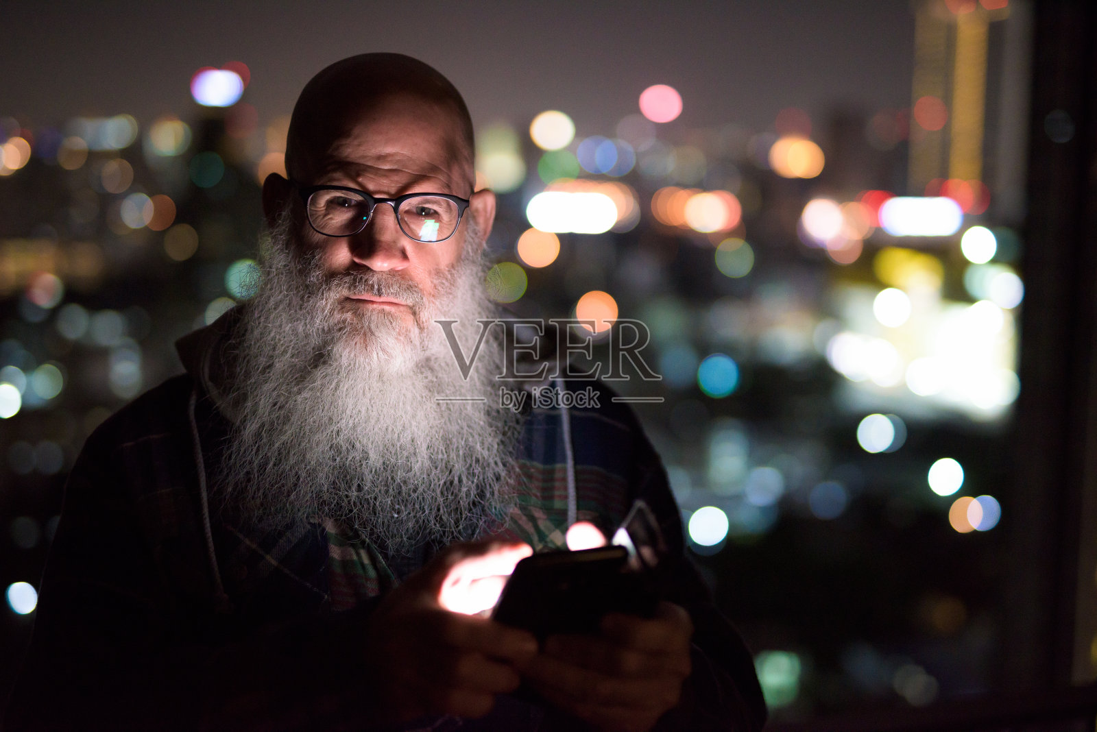 成熟的秃头胡子男子在夜间使用手机对抗城市的景色照片摄影图片