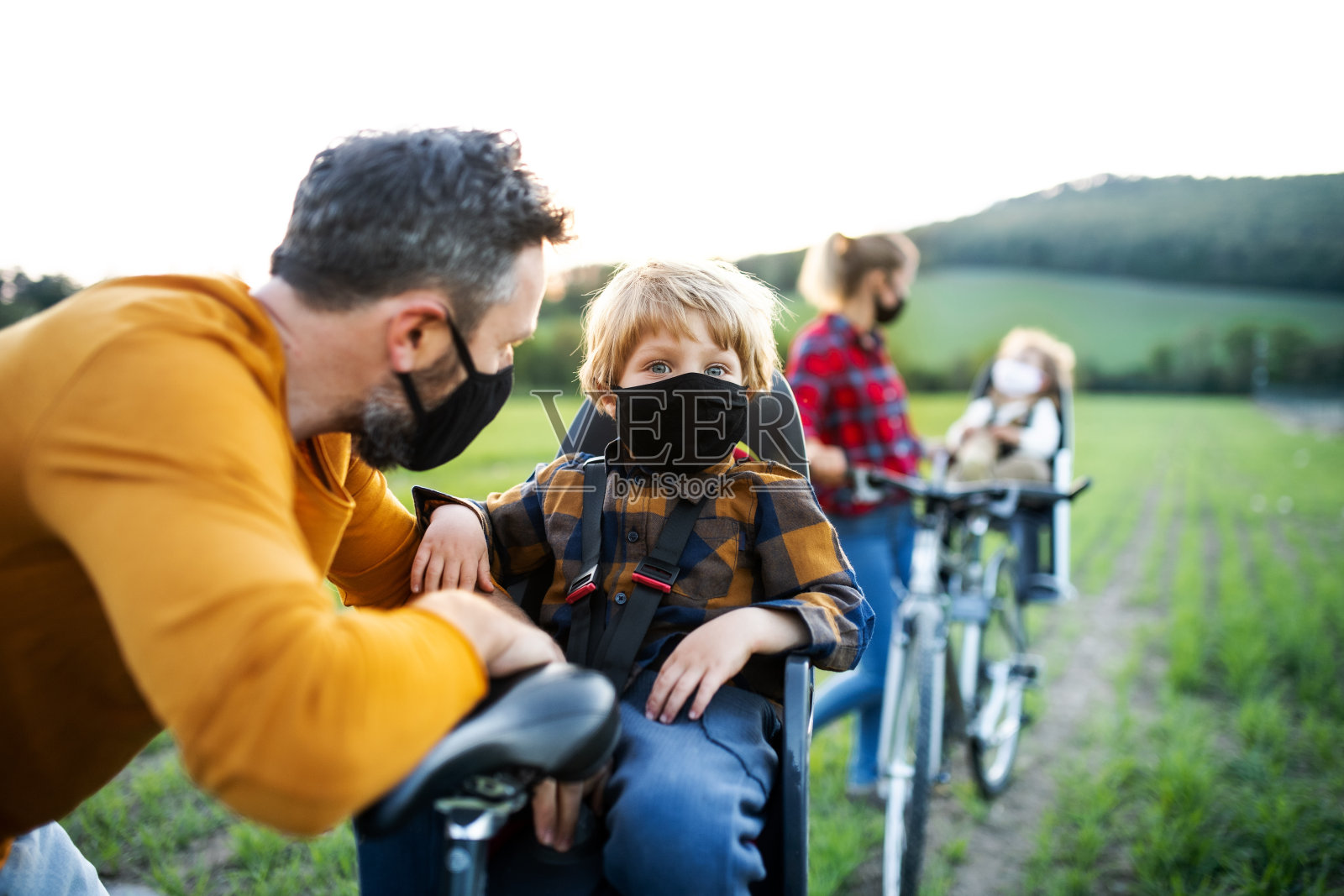 一家人带着两个小孩骑自行车旅行，戴着口罩。照片摄影图片