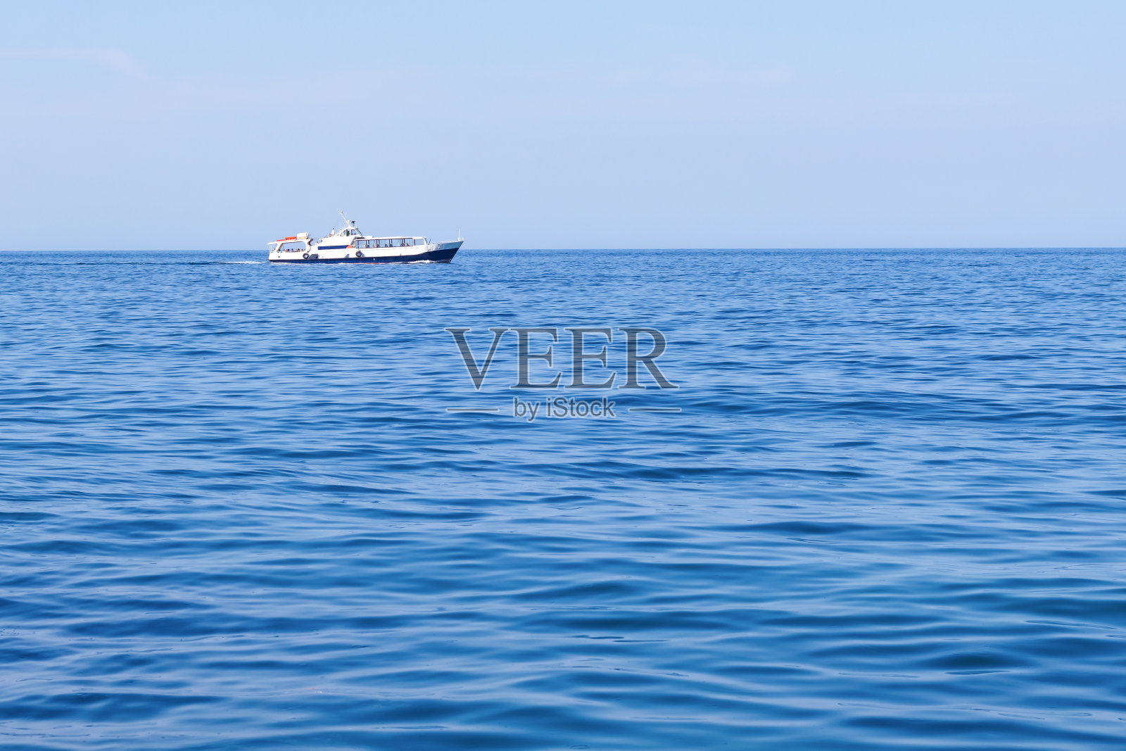 在一个晴朗的日子里，一艘现代化的白色小轮船载着游客在海上航行照片摄影图片