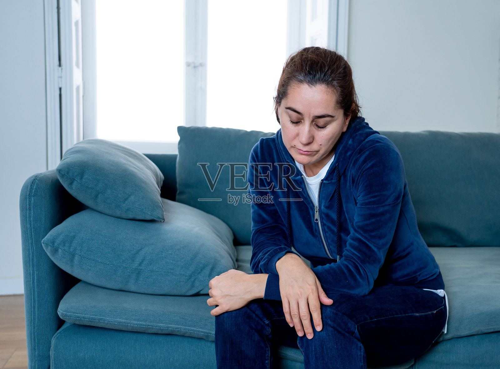 孤独的拉丁女人在沙发上哭泣，感到悲伤疲惫和担忧，遭受抑郁，在家中隔离。精神健康、封锁、压力、失业和心碎概念照片摄影图片