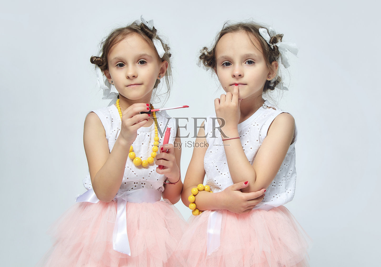 两个小女孩在玩妈妈的化妆品。他们装模作样，试图成为成年人。工作室,白色背景照片摄影图片