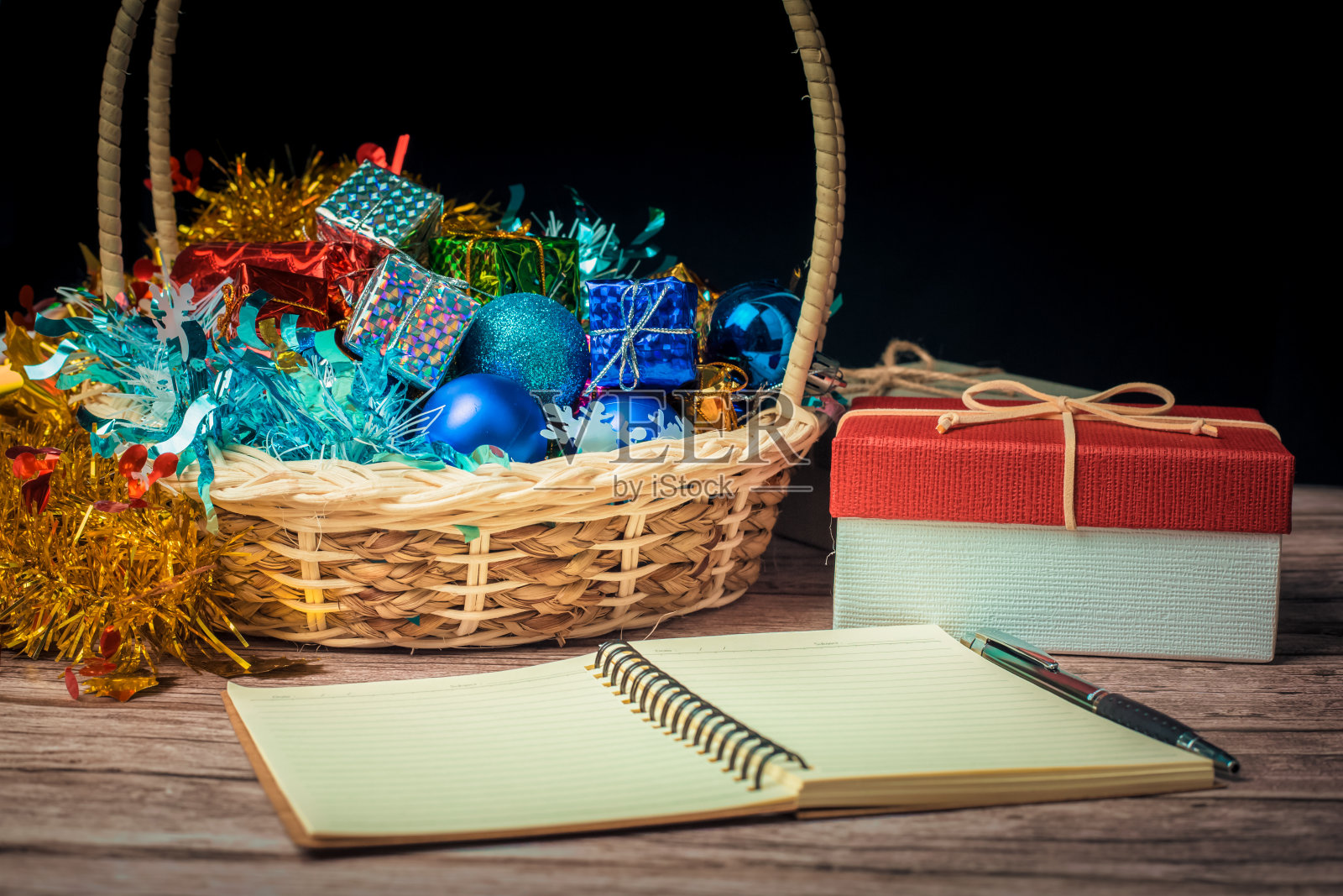 纸笔记本和钢笔和圣诞礼物盒与一些彩色纸和玩具篮子在木桌子上。照片摄影图片