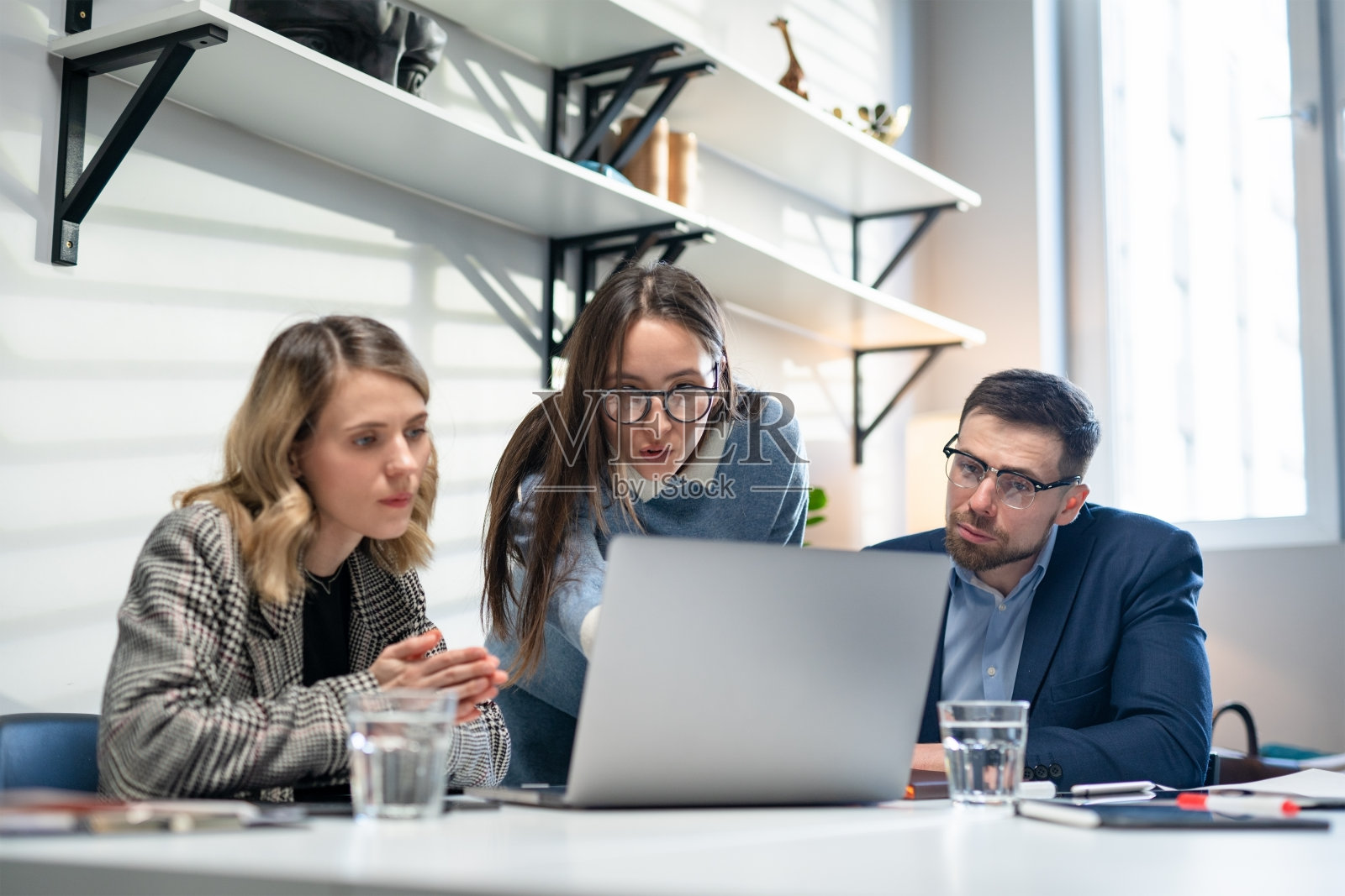 同事和客户用笔记本电脑和平板电脑谈论策略。在创意办公室里，高效的同事们站在公司会议桌前。团队合作与社会观念照片摄影图片