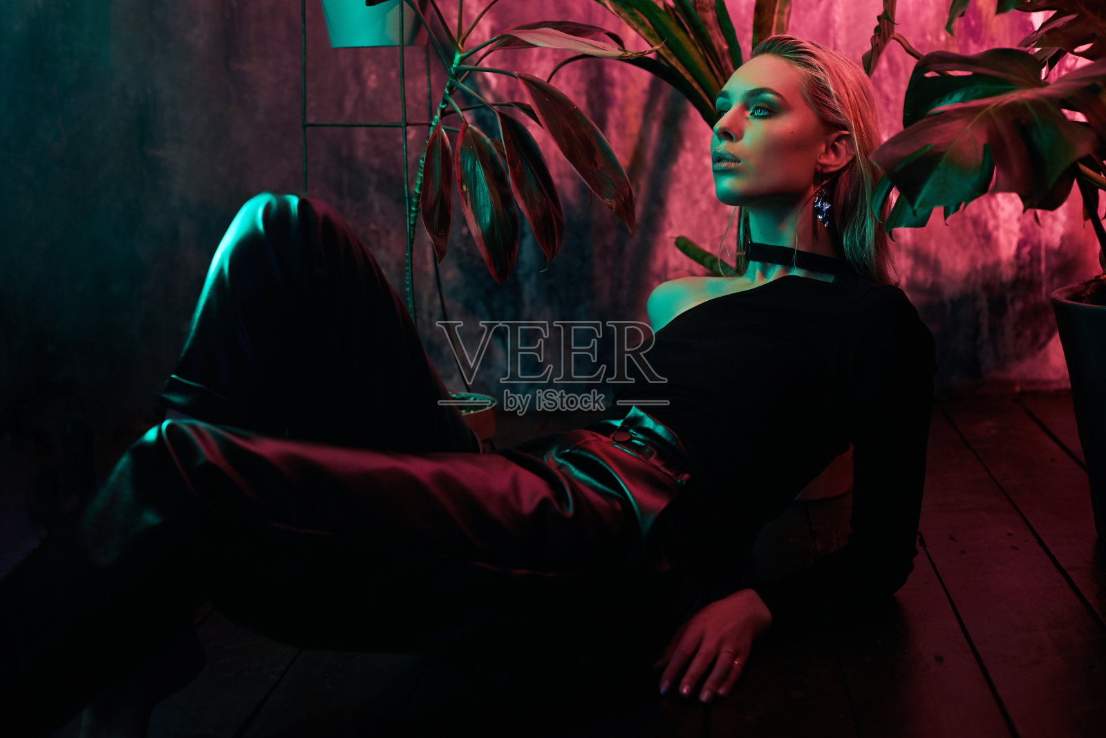时尚的女人坐在地板上的热带树叶霓虹灯。湿润的头发，完美的身材和妆容。粉红色和绿色的霓虹色。美丽的女孩和怪物离开了。照片摄影图片
