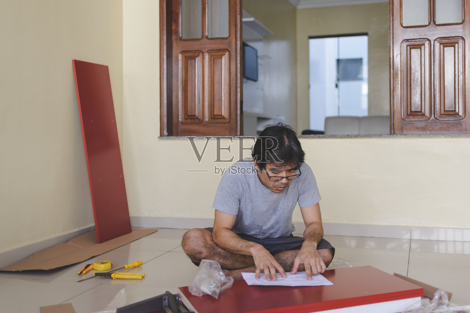 成熟的男子坐在地板上阅读家具组装说明书，在家里DIY照片摄影图片