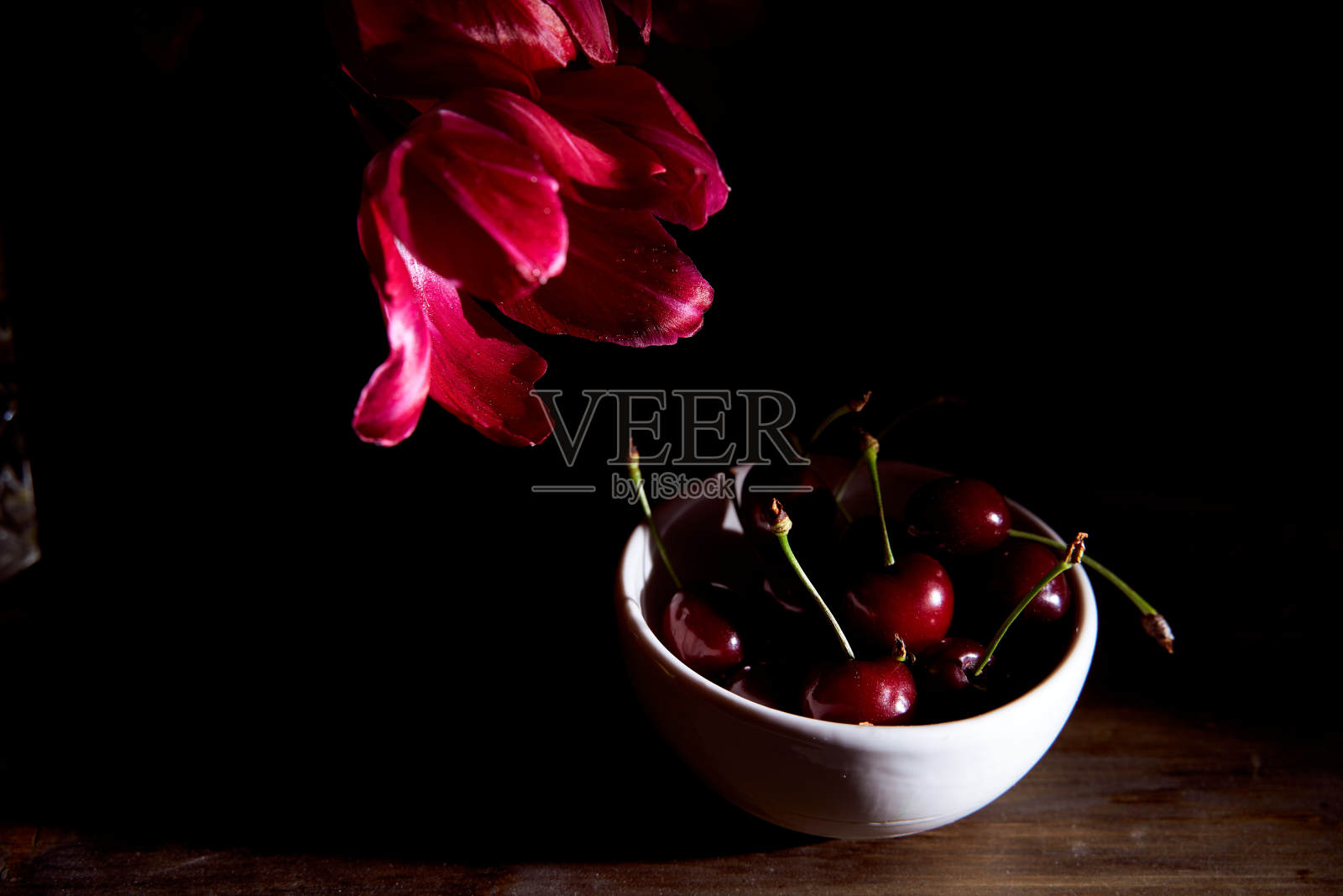 黑色背景下白色杯子里的红樱桃照片摄影图片