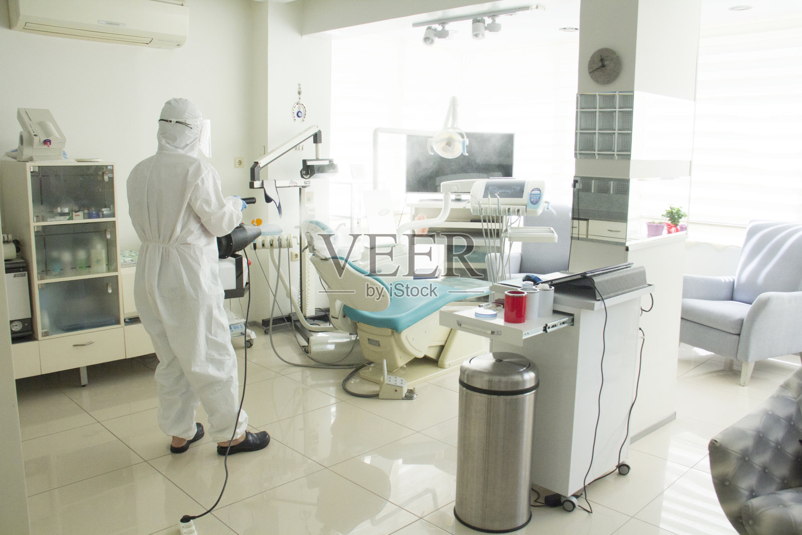 一个穿着防护服的女人在办公室，工作场所，牙医，医生的办公室里消毒。照片摄影图片