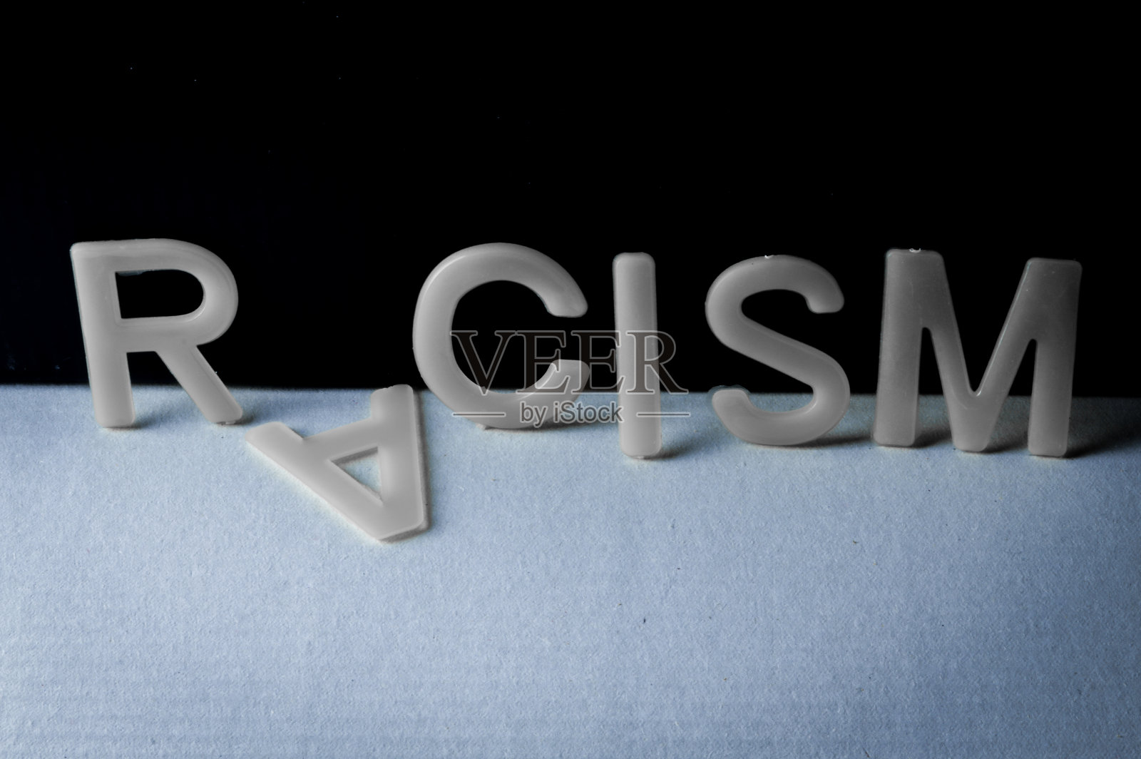 Drop racism(种族主义)一词写在双色调背景上，第二个字母就掉了。反对种族主义的概念。照片摄影图片