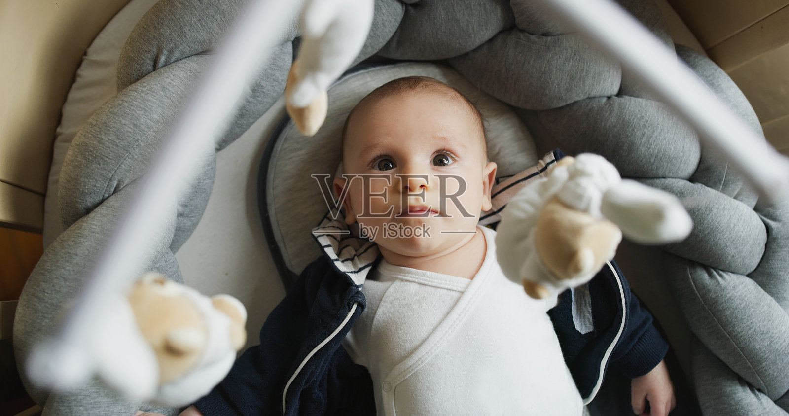 一个可爱的新生婴儿在婴儿室的婴儿床里看着一个音乐旋转台玩手机和微笑的真实特写。照片摄影图片