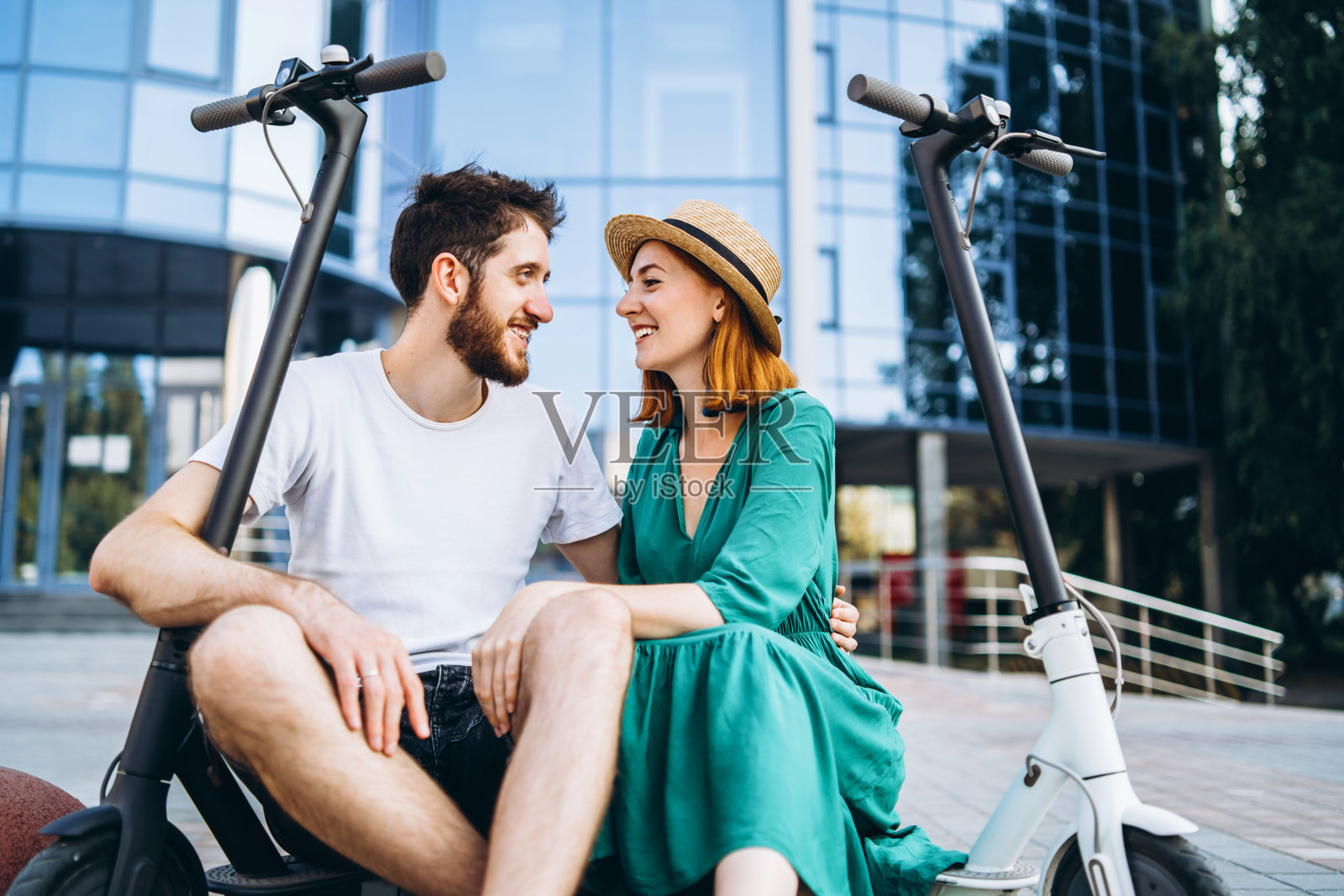 两个有魅力的人正在玻璃建筑附近骑着他们的电动摩托车。男人和女人都喜欢度假照片摄影图片