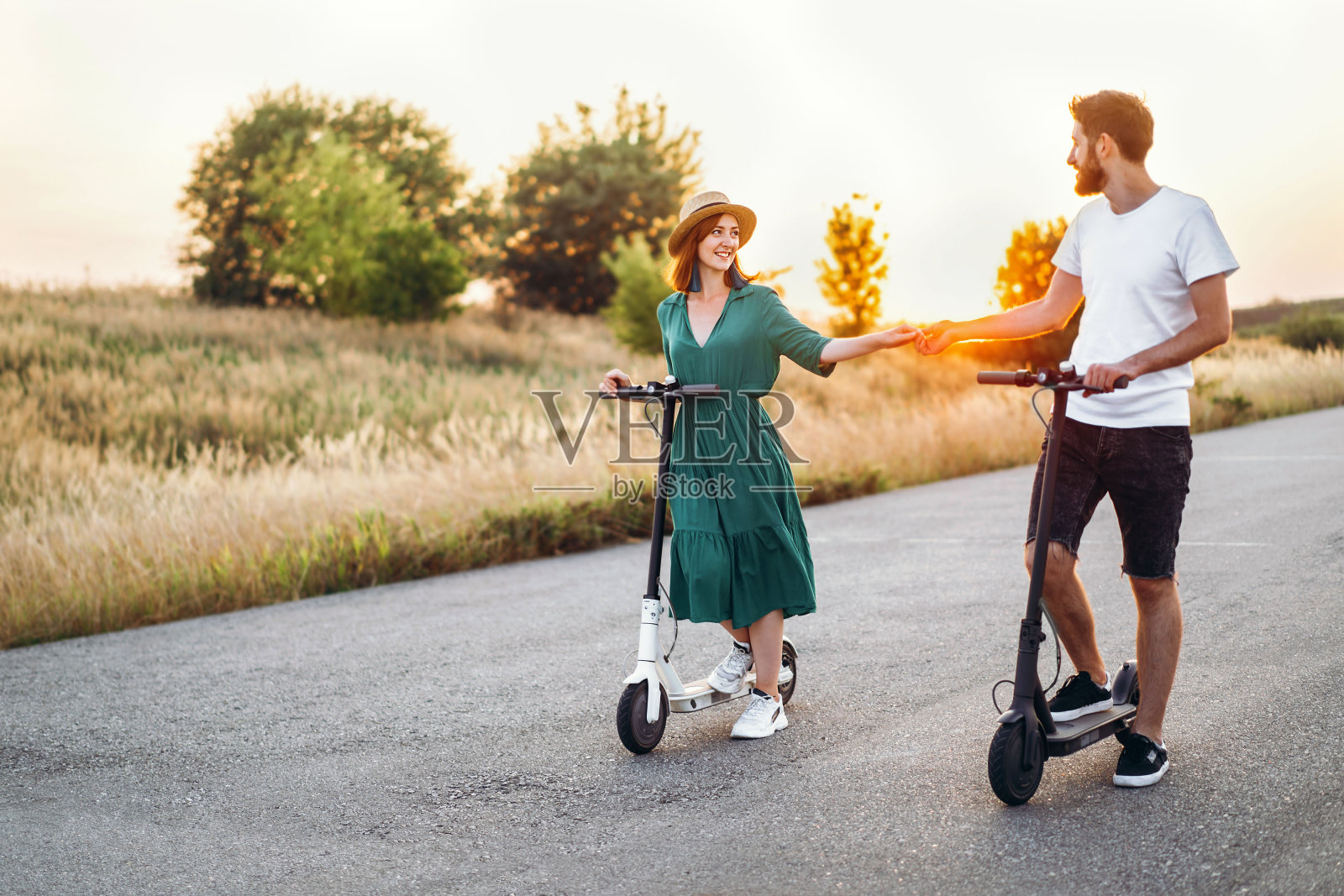 男人和女人牵着手。背景道路和日落。用电动踏板车走路照片摄影图片