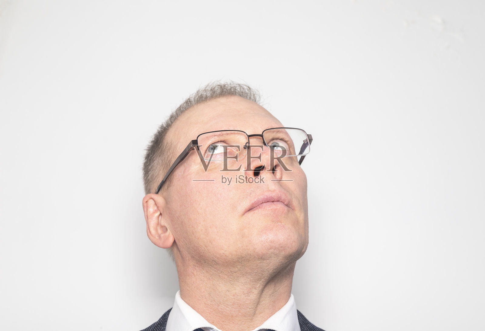 这是一幅沉思的中年资深商人的肖像，他抬头对自己的新想法感到疑惑。在白色背景上隔离照片摄影图片
