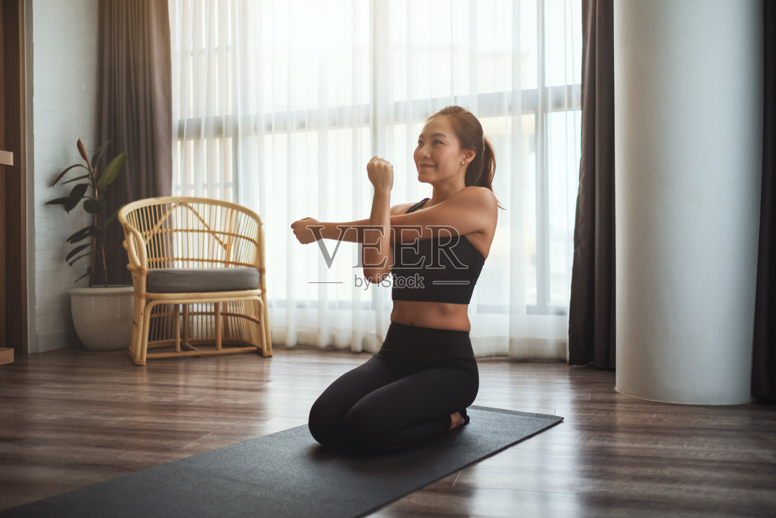 一个美丽的年轻亚洲女子坐在训练垫和伸展她的手臂热身之前，在家里锻炼照片摄影图片