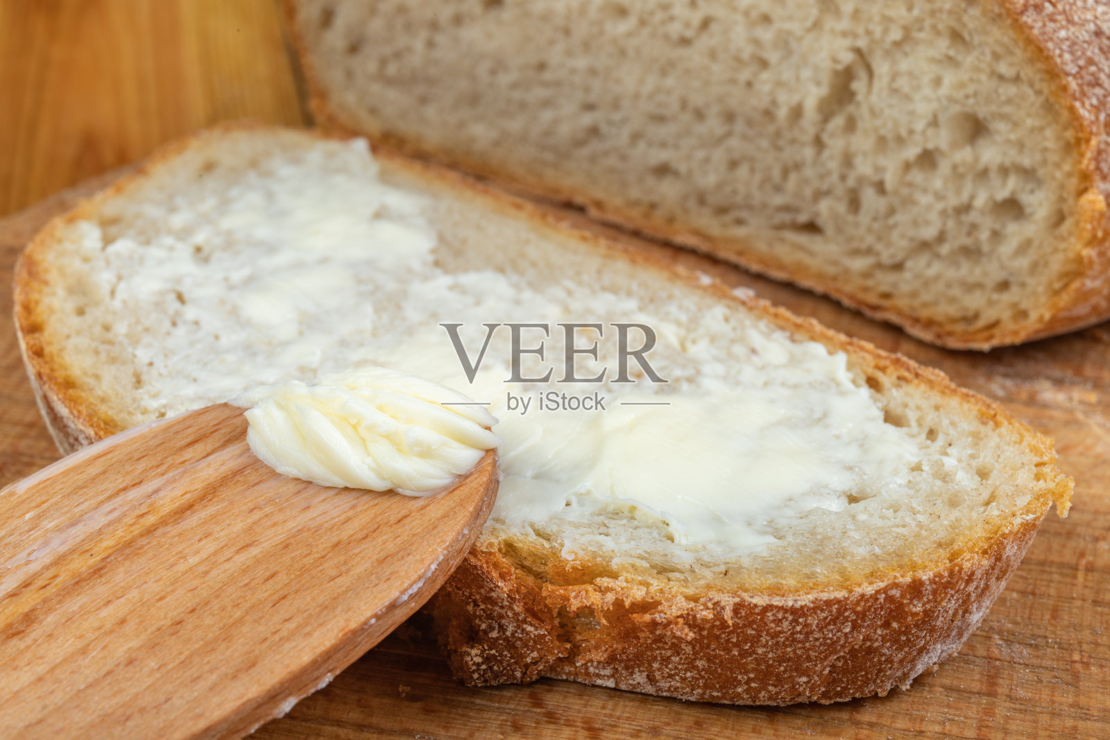 涂在新鲜面包上的黄油。家庭厨房里的面包。黑暗的背景。照片摄影图片