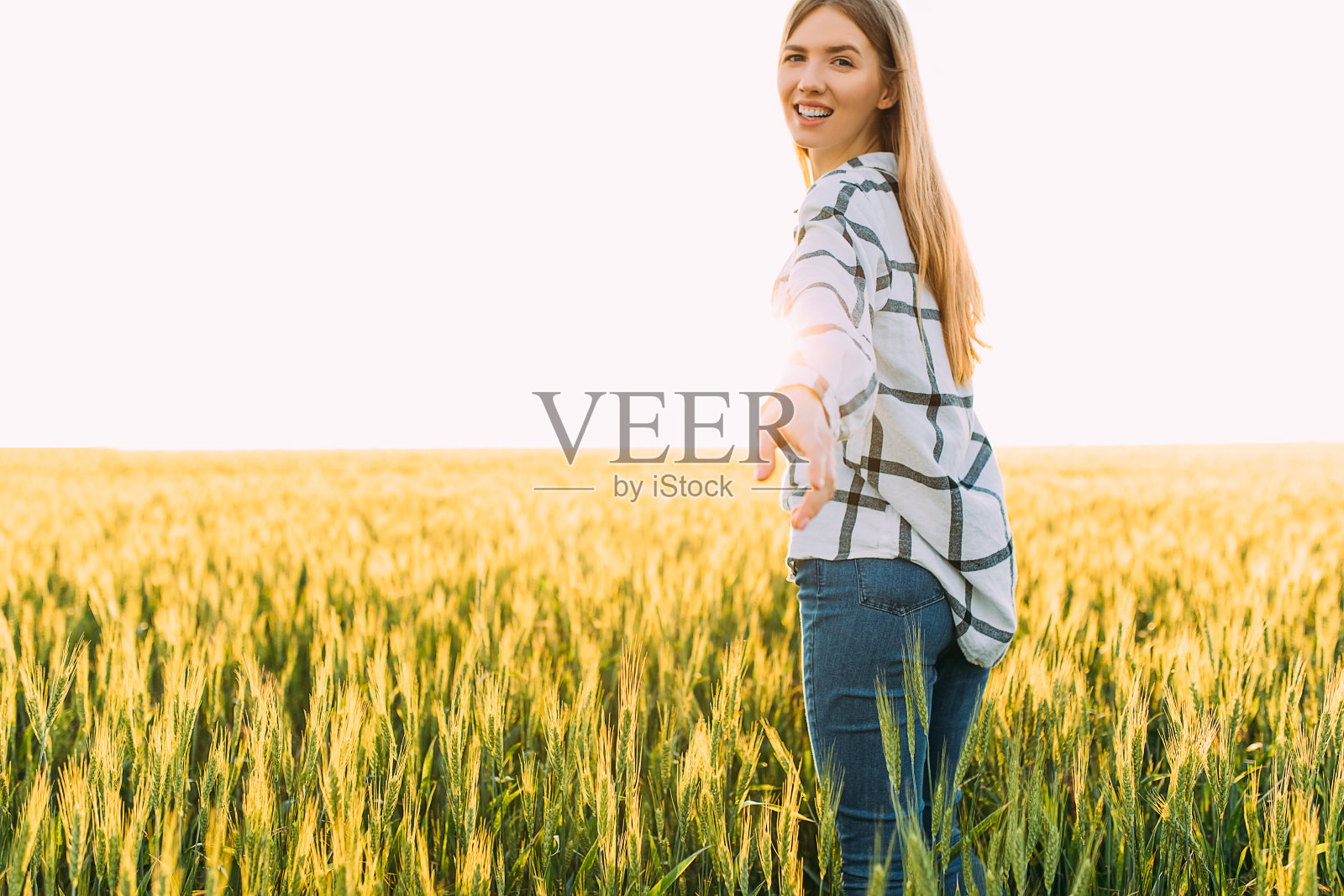 在阳光明媚的夕阳下，快乐的女人穿着格子衬衫在麦田里漫步照片摄影图片