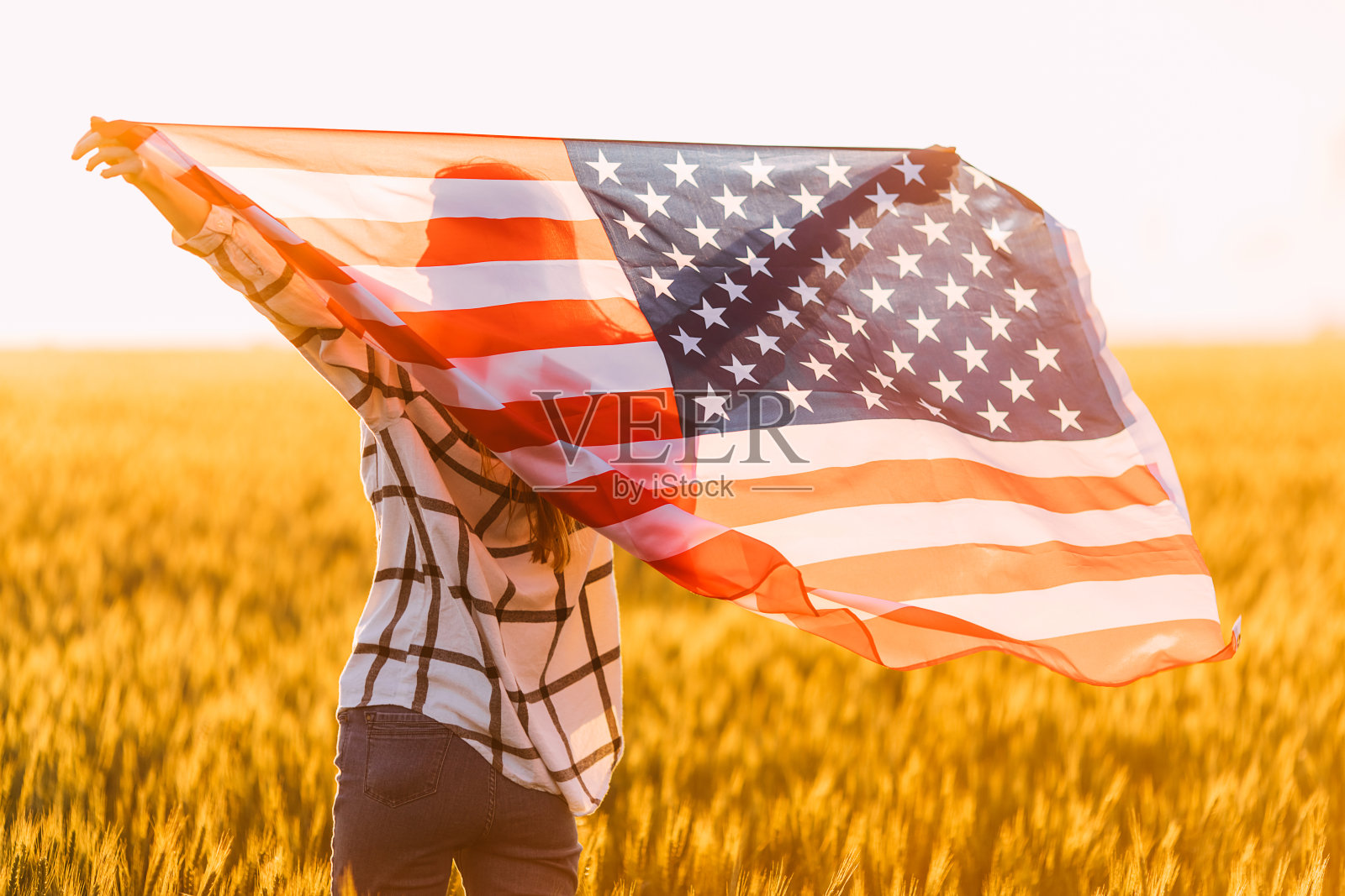 迷人的快乐的女人，在麦田与美国国旗的背景日落照片摄影图片