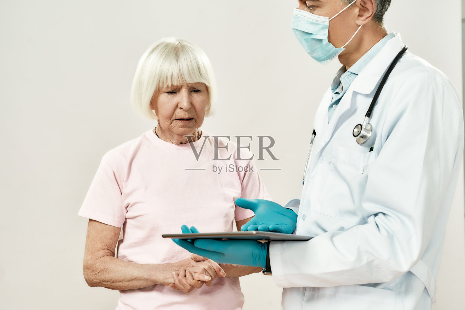 坏消息。成熟的男医生穿着医疗制服，戴着防护口罩解释诊断，与心烦意乱的年长女病人说话。医疗横幅照片摄影图片