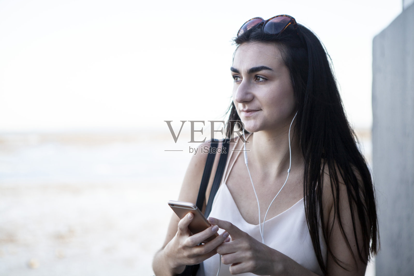 一个少女在夏天靠在墙上用智能手机，背景是大海照片摄影图片
