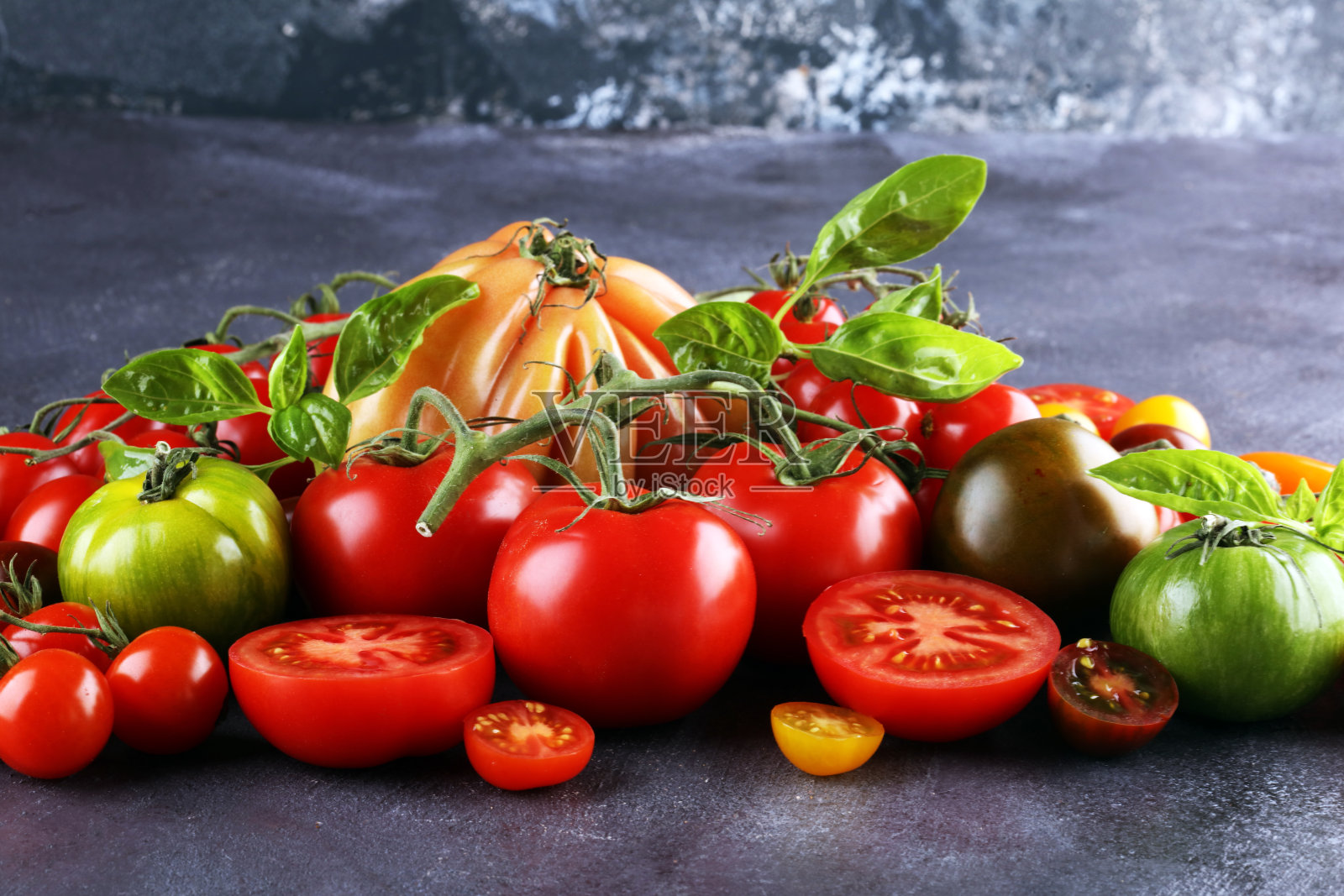 质朴的餐桌上放着五颜六色的西红柿和罗勒叶。照片摄影图片