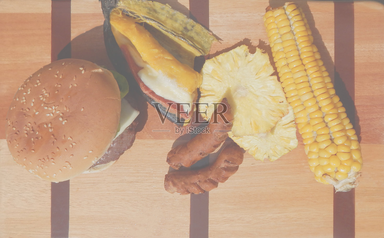 用玉米、香蕉、菠萝和香肠铺在木板上的自制汉堡照片摄影图片