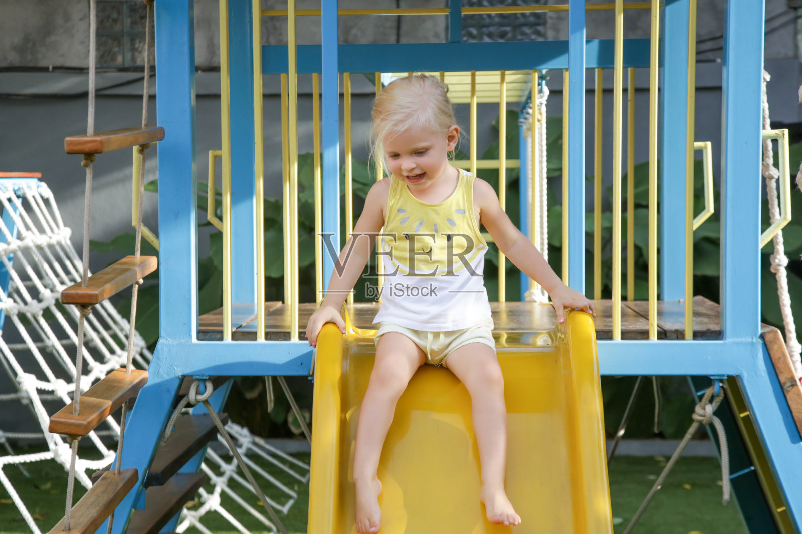活泼的蹒跚学步的女孩在滑梯上。孩子们在户外操场上玩耍。儿童健康的夏季活动。孩子们在学校或幼儿园的院子里玩耍。照片摄影图片