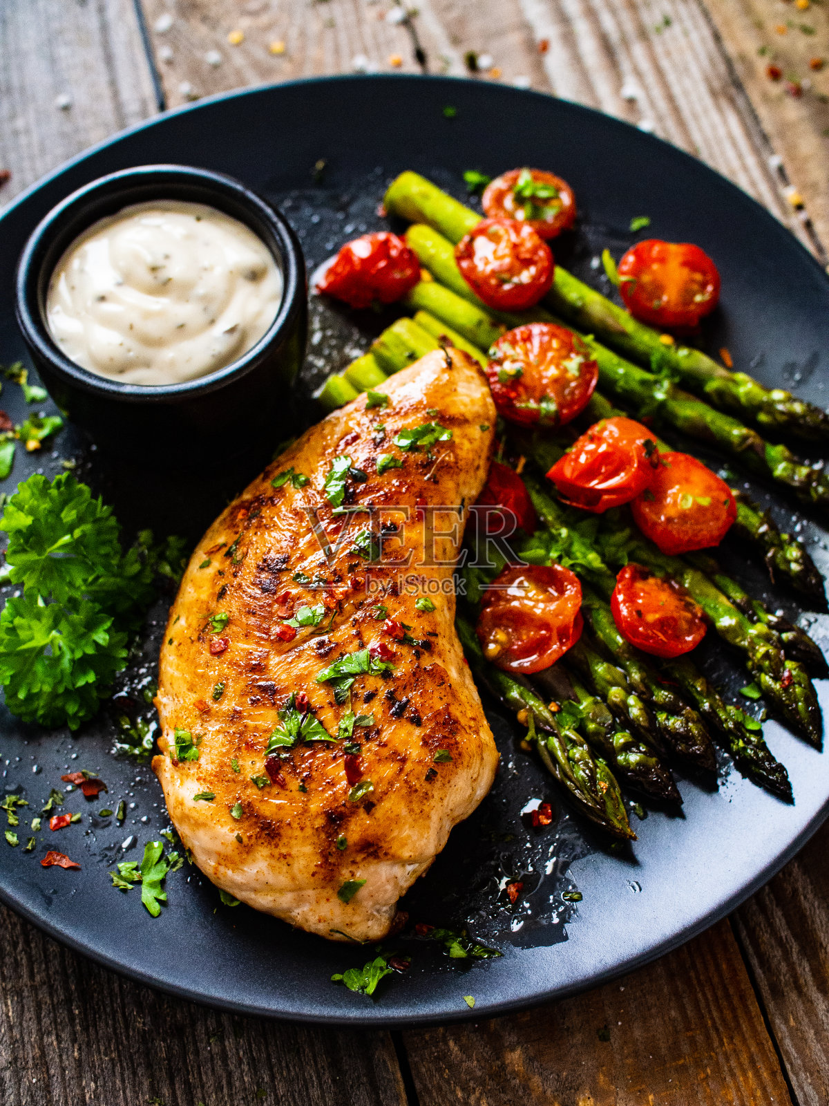 炸鸡胸肉配芦笋和圣女果，摆放在黑色盘子上照片摄影图片