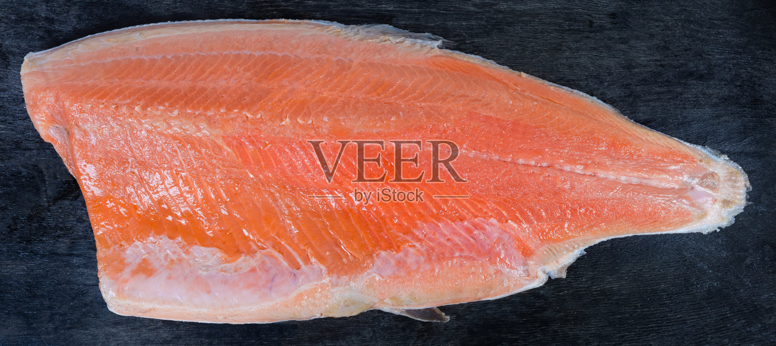 鳟鱼鱼片的外皮朝下在黑色的表面照片摄影图片