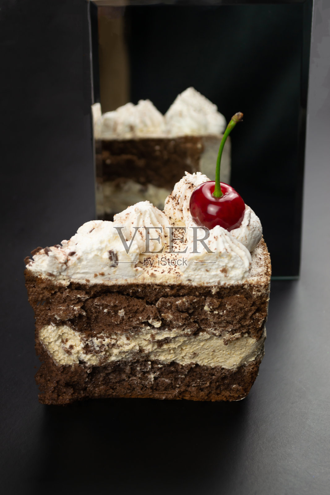 用樱桃装饰的三角形提拉米苏在没有樱桃的情况下反射在镜子上。照片摄影图片