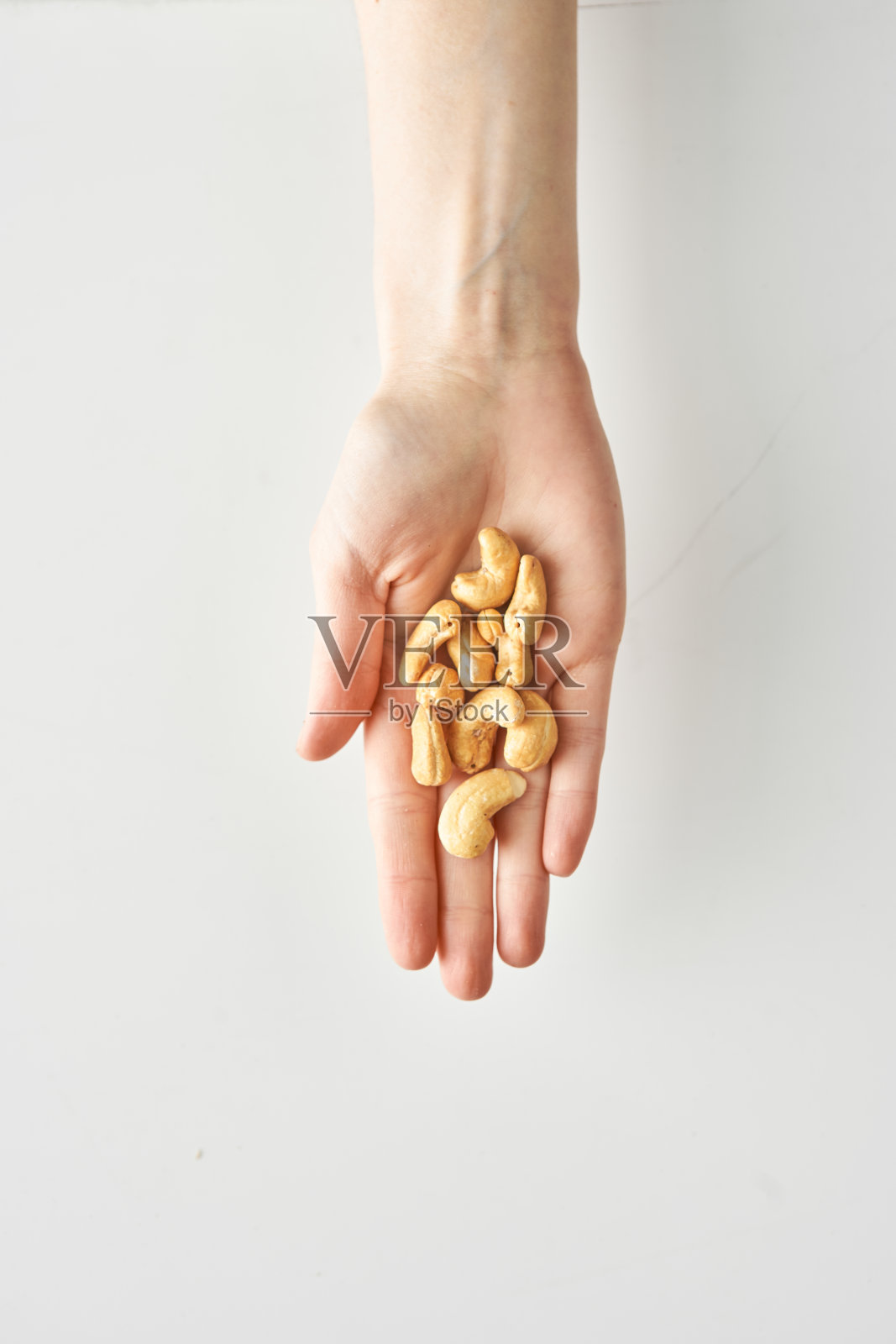 100卡路里的腰果在一个女人的手上孤立的白色背景，健康的食物和生活方式照片摄影图片