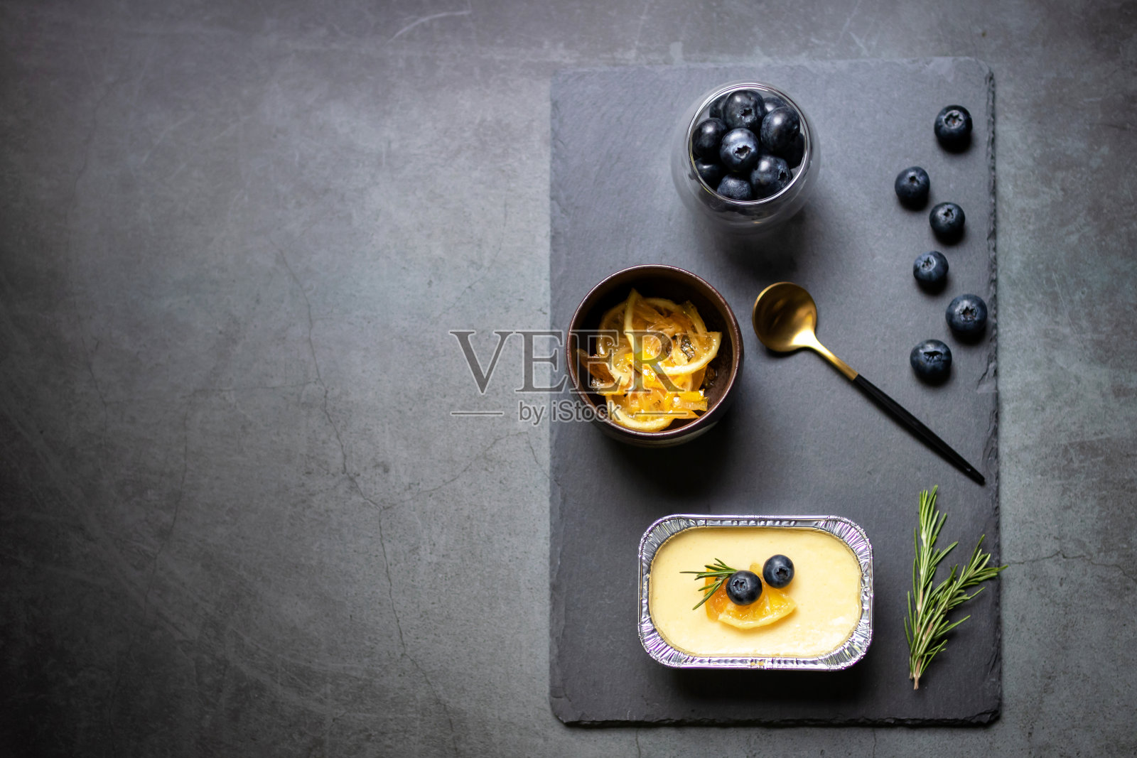 自制芝士蛋糕与新鲜蓝莓和蜜饯柠檬在黑石背景。照片摄影图片