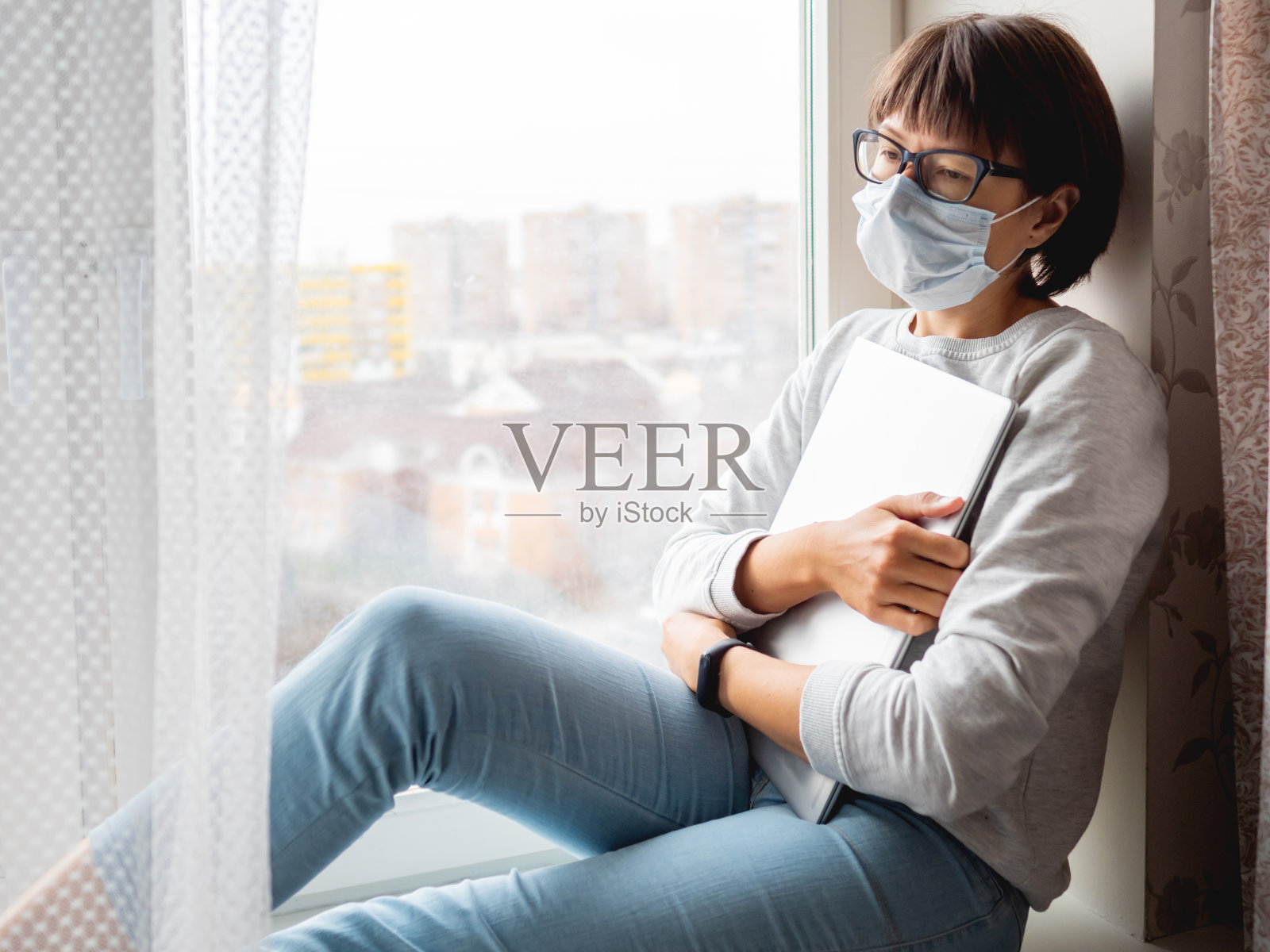 一个戴医用口罩的女人丢了工作。她坐在窗台上，手提电脑关着。因冠状病毒感染而实施封锁隔离。在家里自我隔离。照片摄影图片