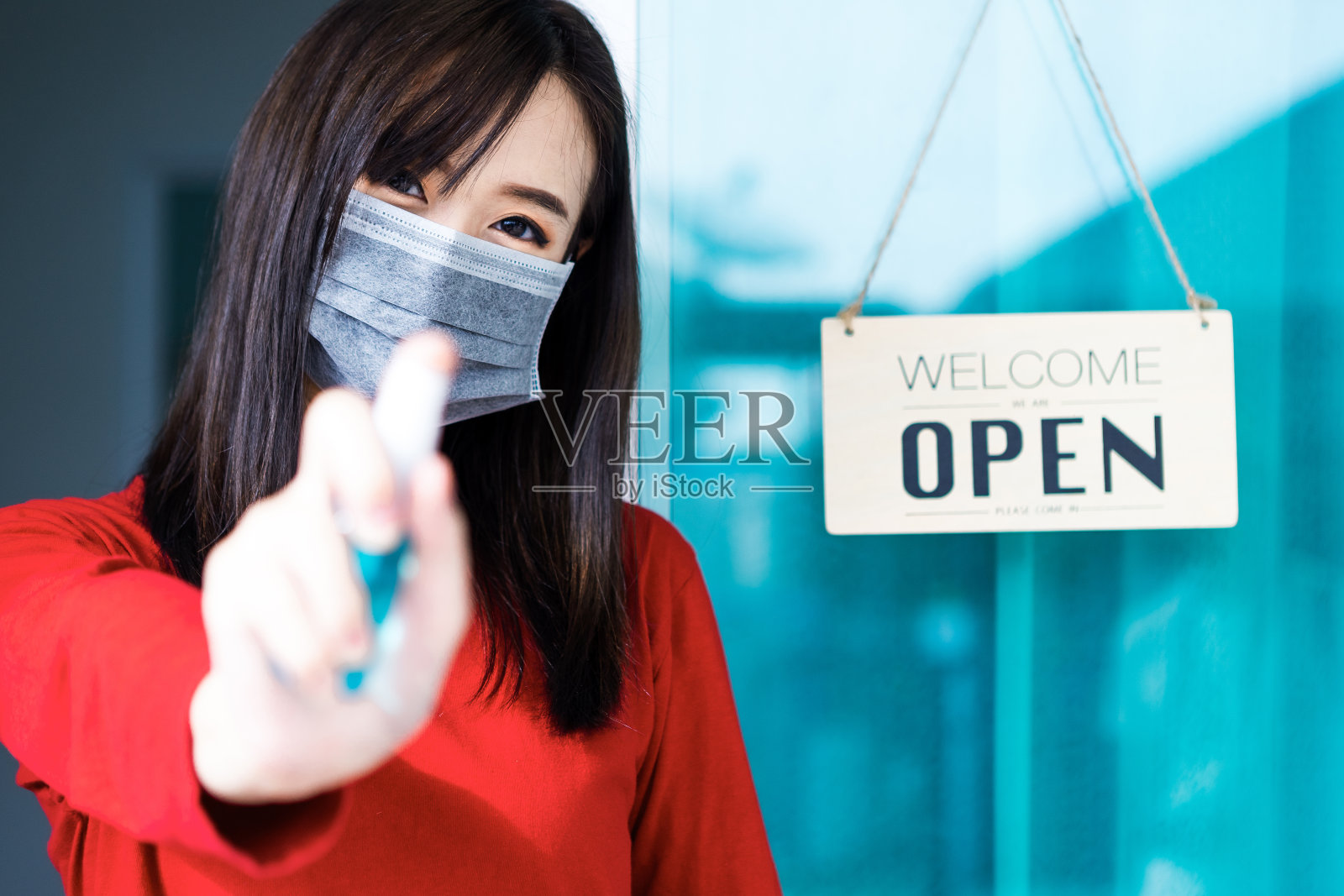 亚洲女店主微笑着挂着“欢迎，我们开门了”的标签，并鼓起掌来。她是在冠状病毒大流行后开店的照片摄影图片