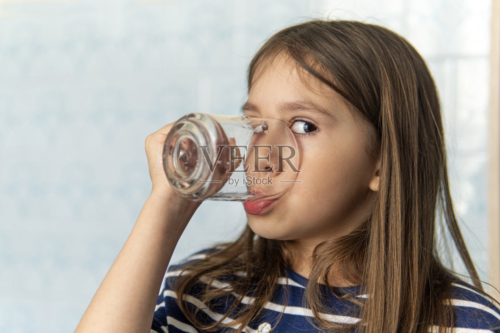 小女孩拿着一杯水。一个小女孩用玻璃杯喝水。渴。照片摄影图片