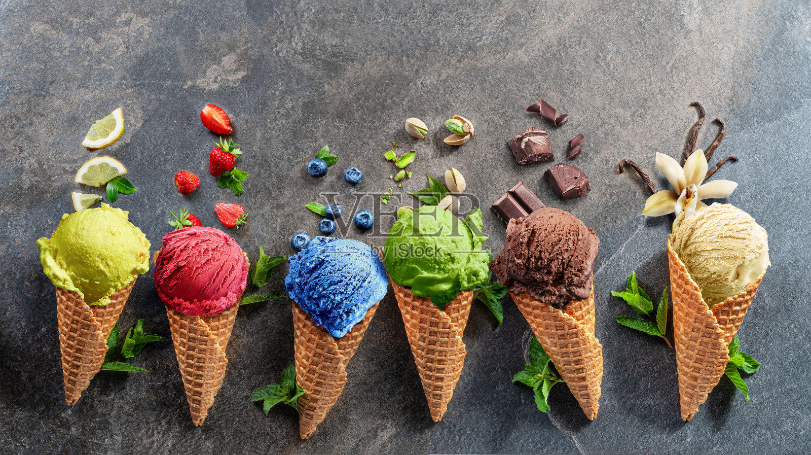 一套各种颜色的华夫蛋筒冰淇淋与水果切片在灰色的背景。照片摄影图片