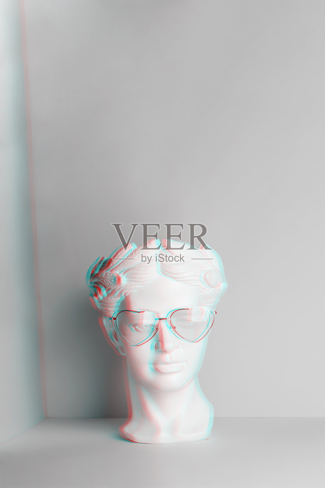 白色雕塑的古董头在粉红色的眼镜与心。两种颜色的几何背景。照片摄影图片